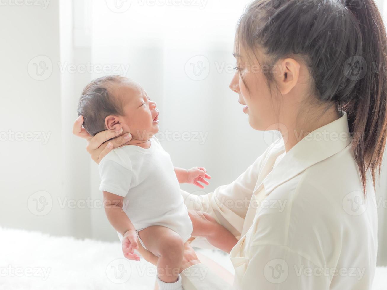 A beautiful Asian woman is looking at her newborn baby with happiness and love photo