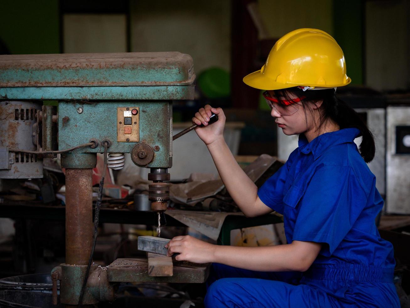 mujeres asiáticas con uniformes mecánicos están usando herramientas eléctricas para perforar barras de metal en la fábrica foto