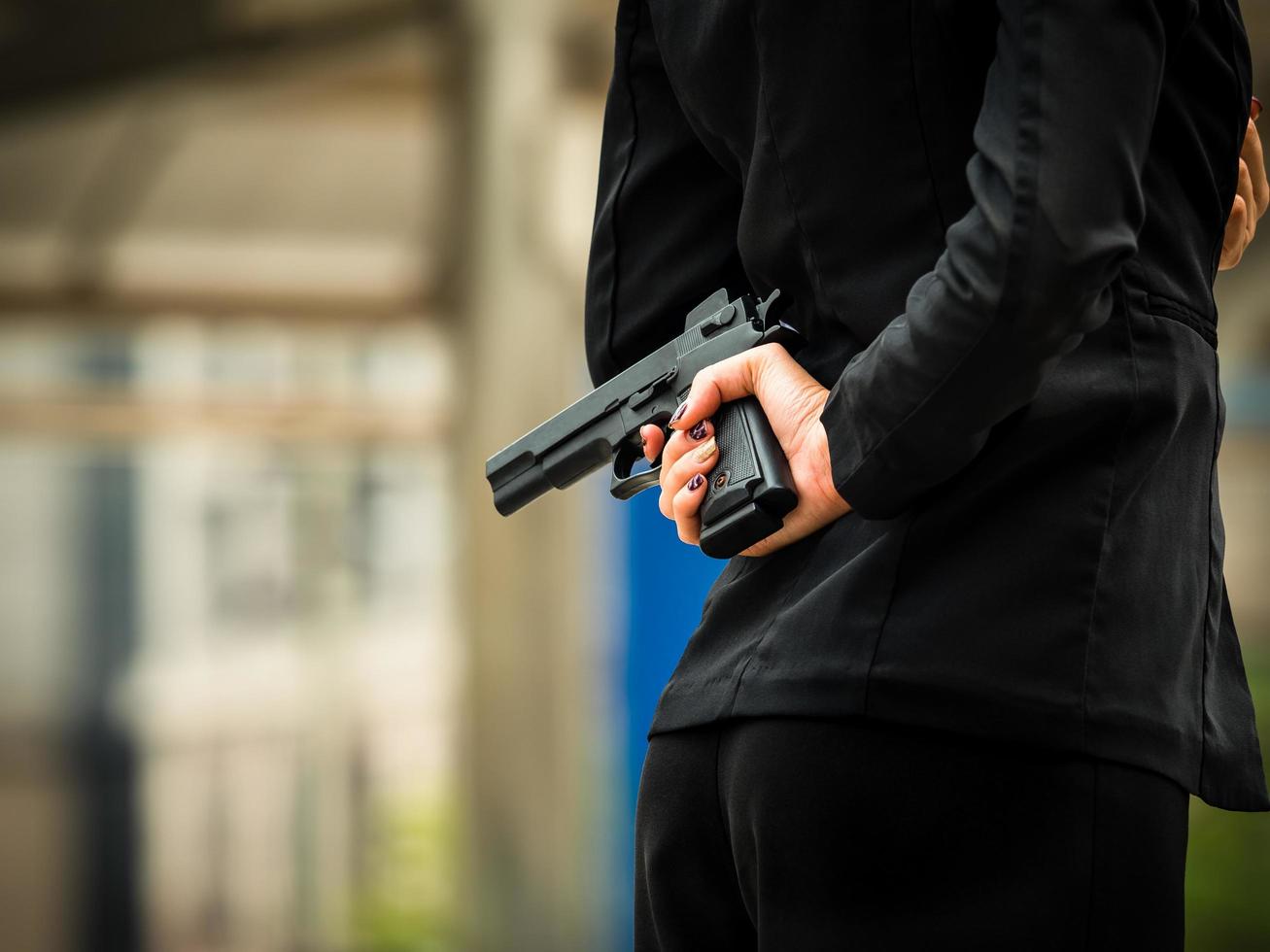 una mujer con traje de negocios sostiene un arma escondida en la espalda, un concepto de traición en los negocios foto