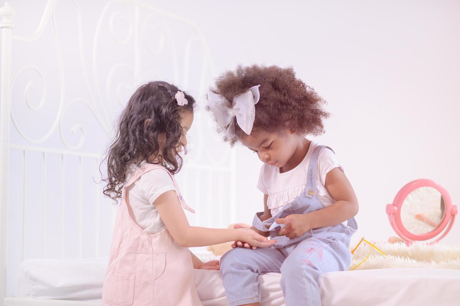 Cute African girl spraying alcohol gel to her Asian friend for cleanliness and prevention of germs photo