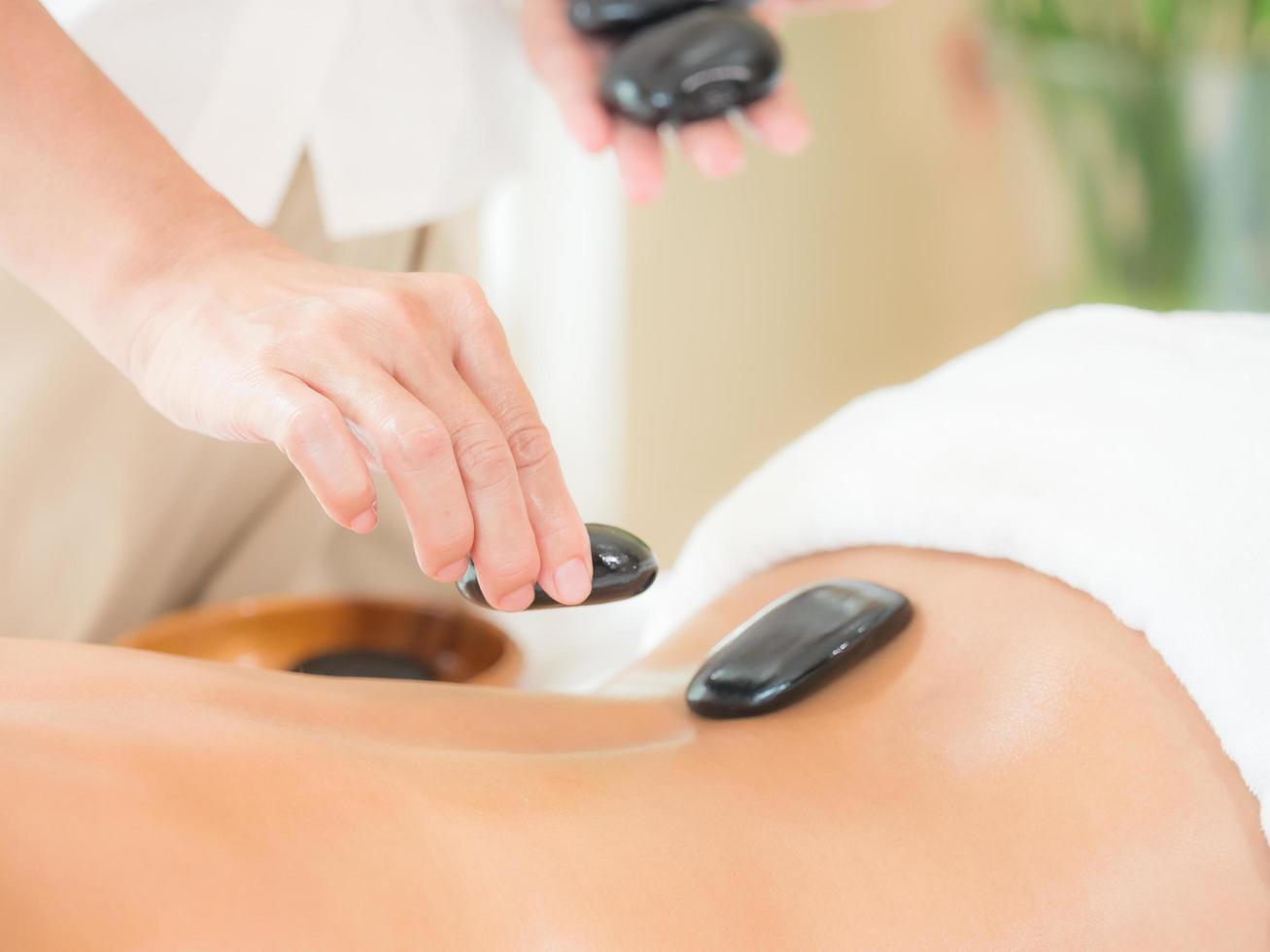 An expert masseuse at a spa salon puts hot stone on the back of an Asian woman to relieve tension from work photo