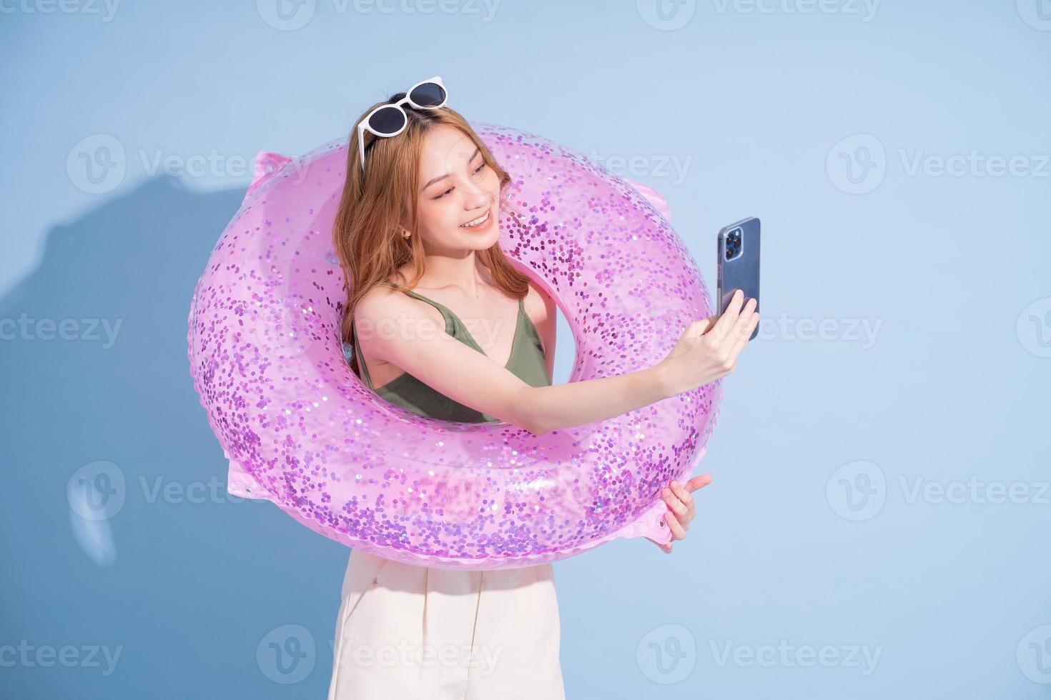 imagen de una joven asiática sosteniendo un flotador sobre fondo azul, concepto de vacaciones de verano foto