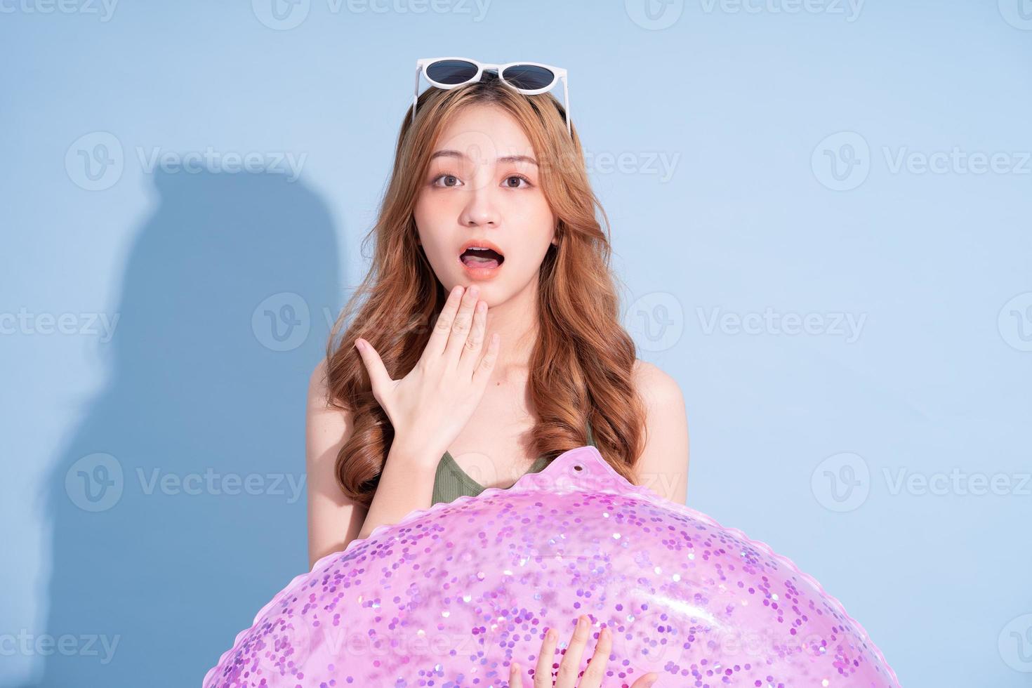 Image of young Asian girl holding swimming float on blue background, summer vacation concept photo