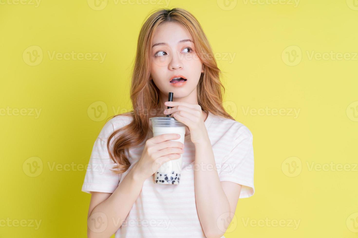 Image of young Asian girl drinking milk tea on yellow background photo