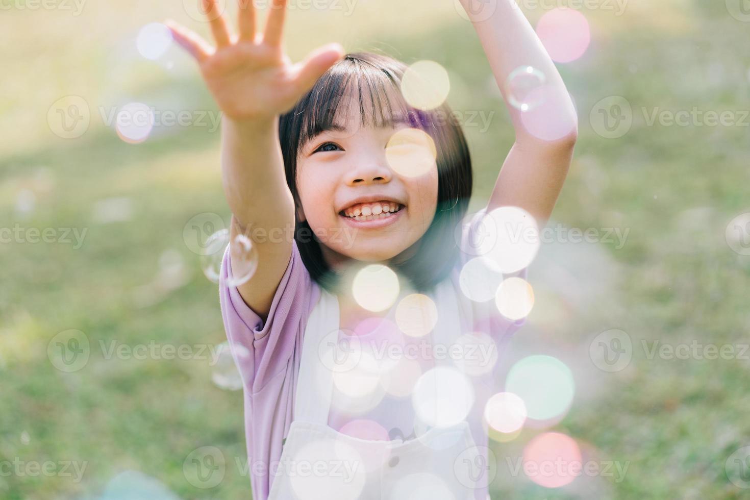Image of Asian little girl playing with soap bubbles at park photo