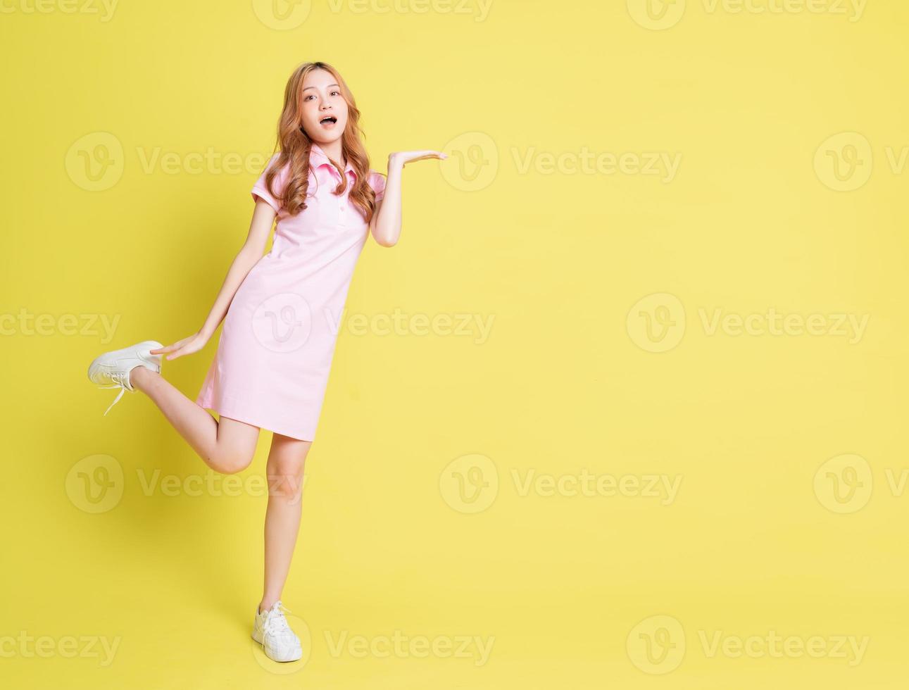 Full length image of young Asian girl standing on yellow background photo