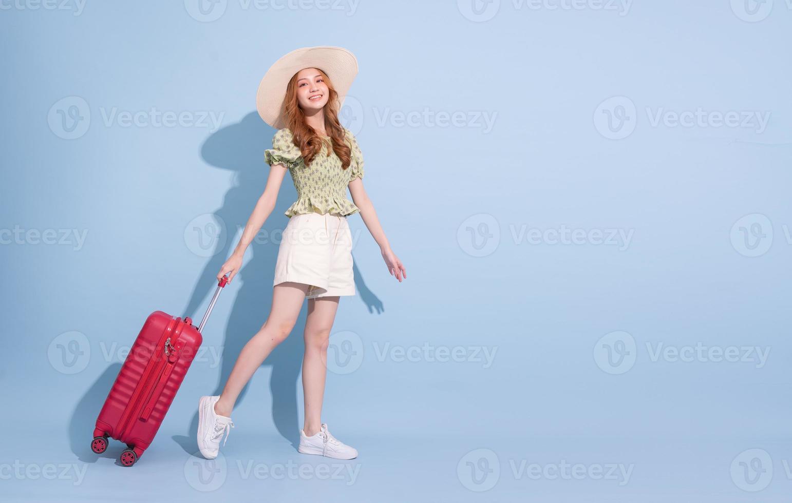 Full length image of young Asian girl with suitcase on blue background, travel concept photo
