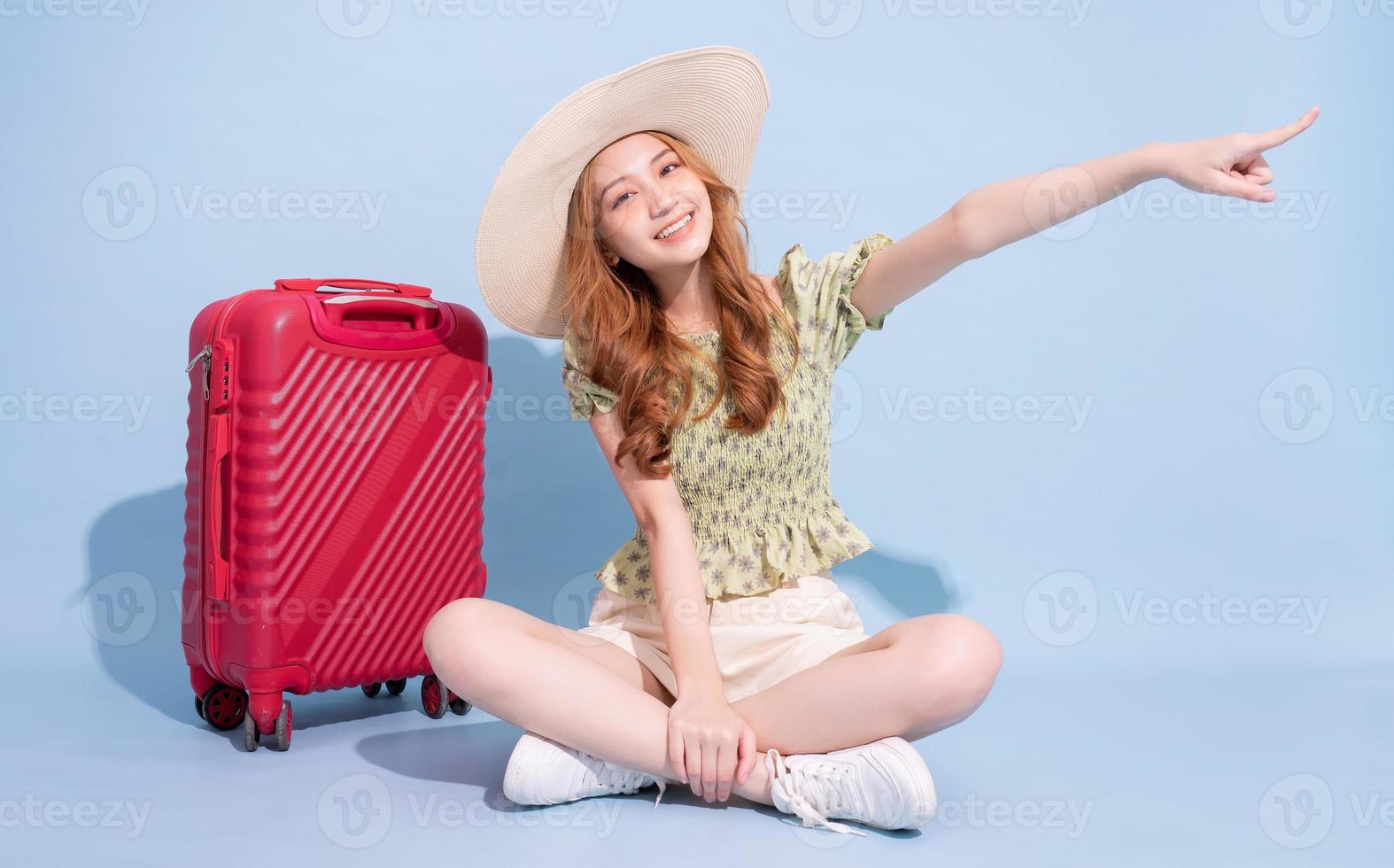 Full length image of young Asian girl with suitcase on blue background, travel concept photo