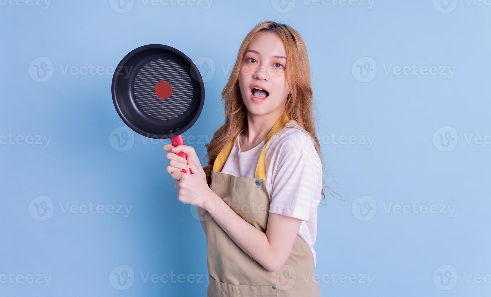 Image of young Asian woman holding pan on blue background photo