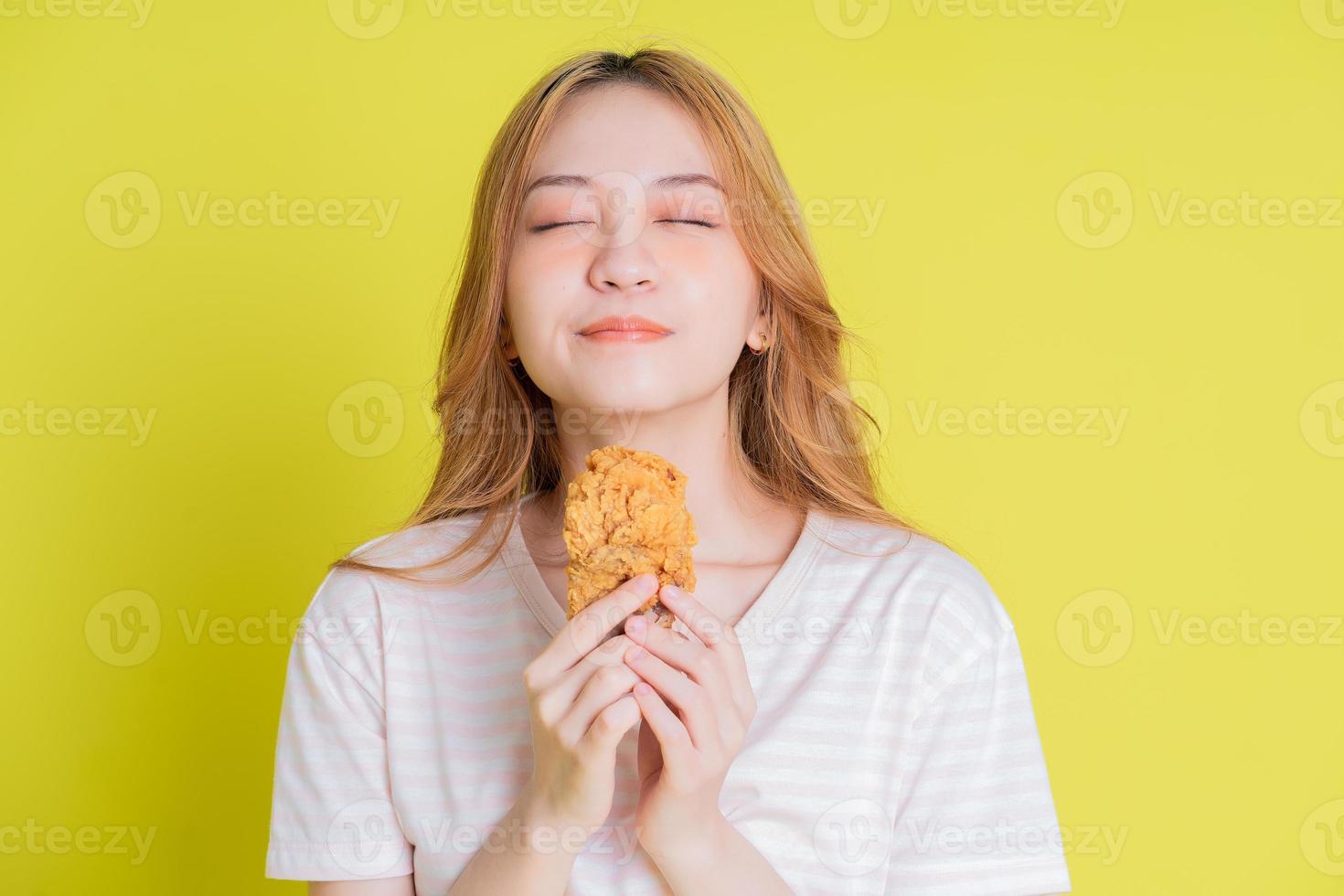 Image of young Asian girl eating chicken fried on yellow background photo