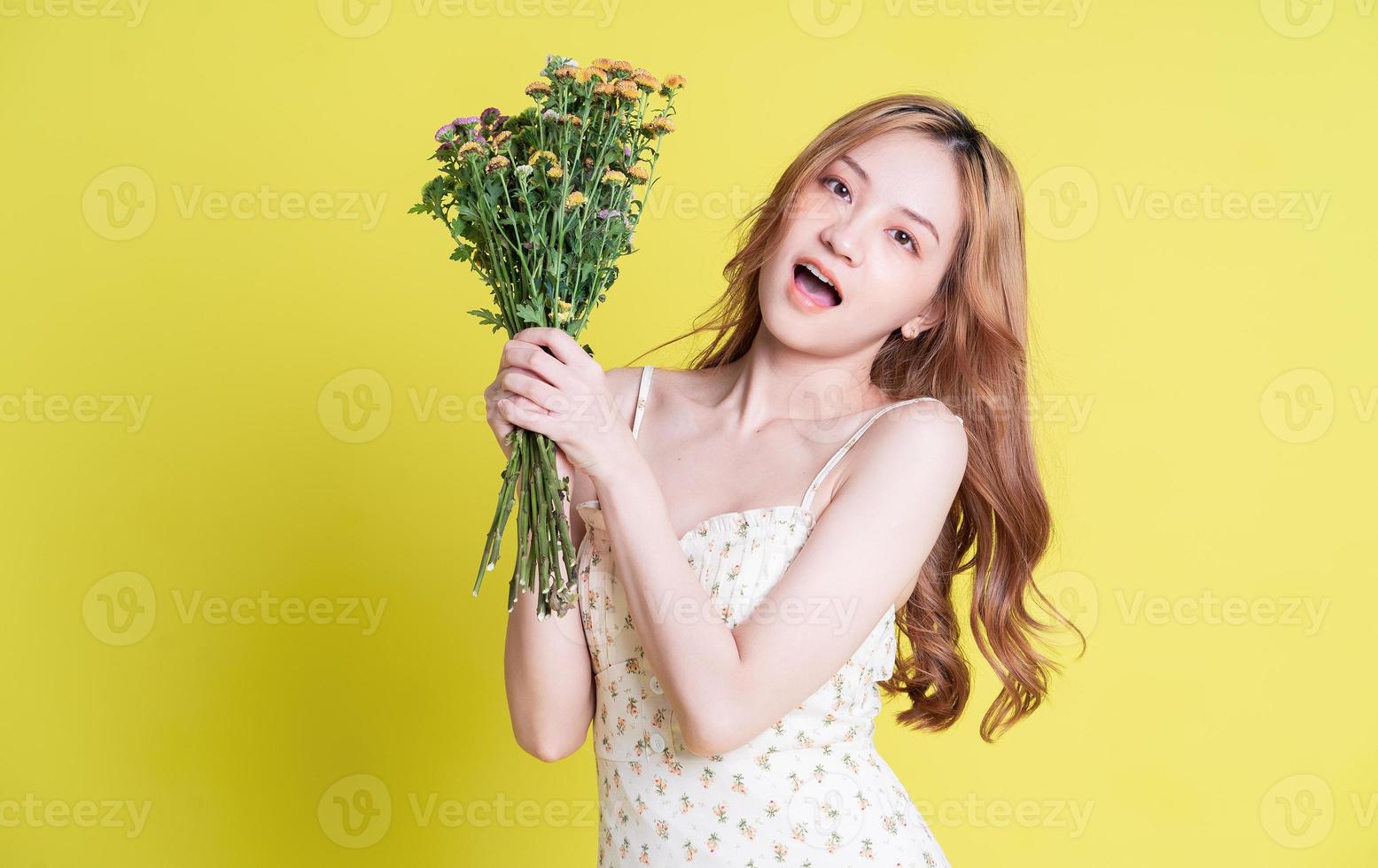 Image of young Asian woman holding flowers on yellow background photo