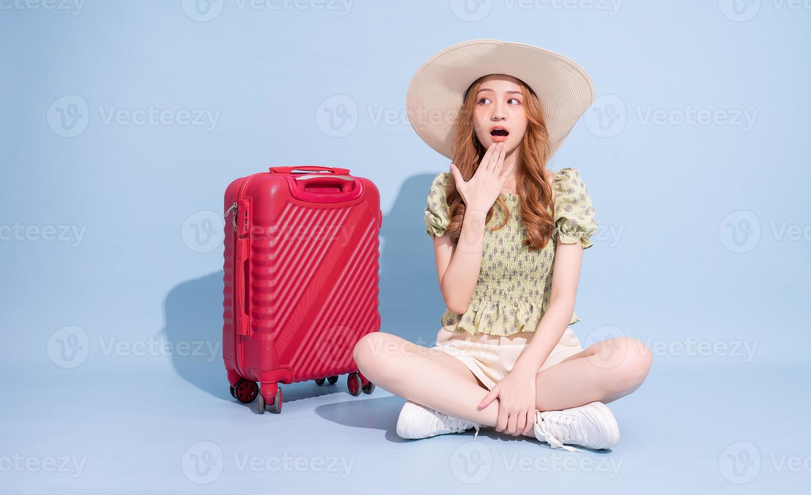 Full length image of young Asian girl with suitcase on blue background, travel concept photo