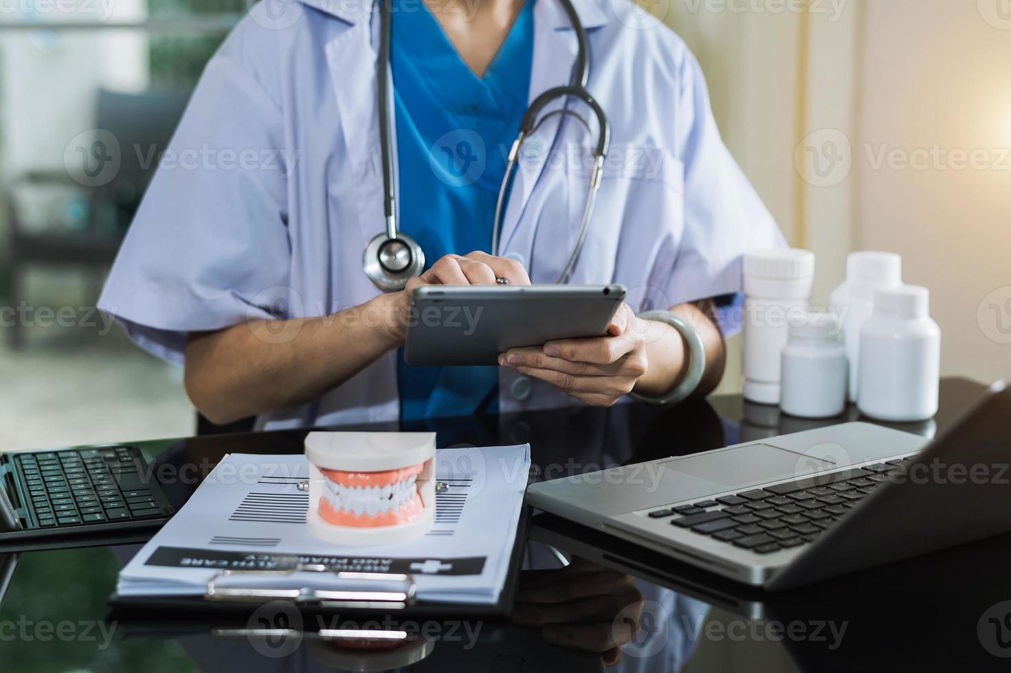 Concentrated dentist sitting at table with jaw samples tooth model and working with tablet and laptop in dental office professional dental clinic. photo