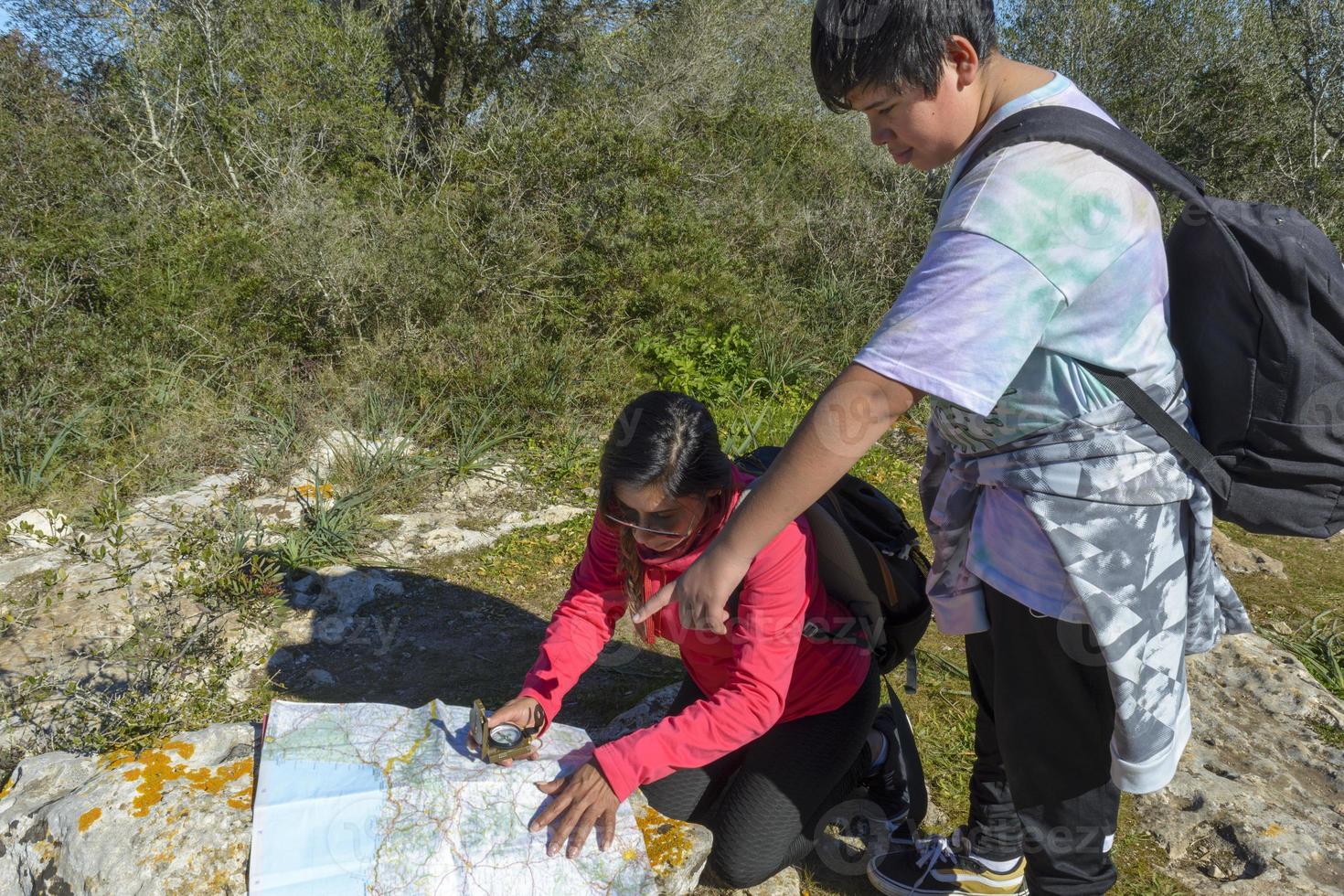 The boy and his mother are standing on top of the mountain. A woman travels with a child. Boy with his mother looking at a map. Travel with backpacks. Walk and climb with children. photo