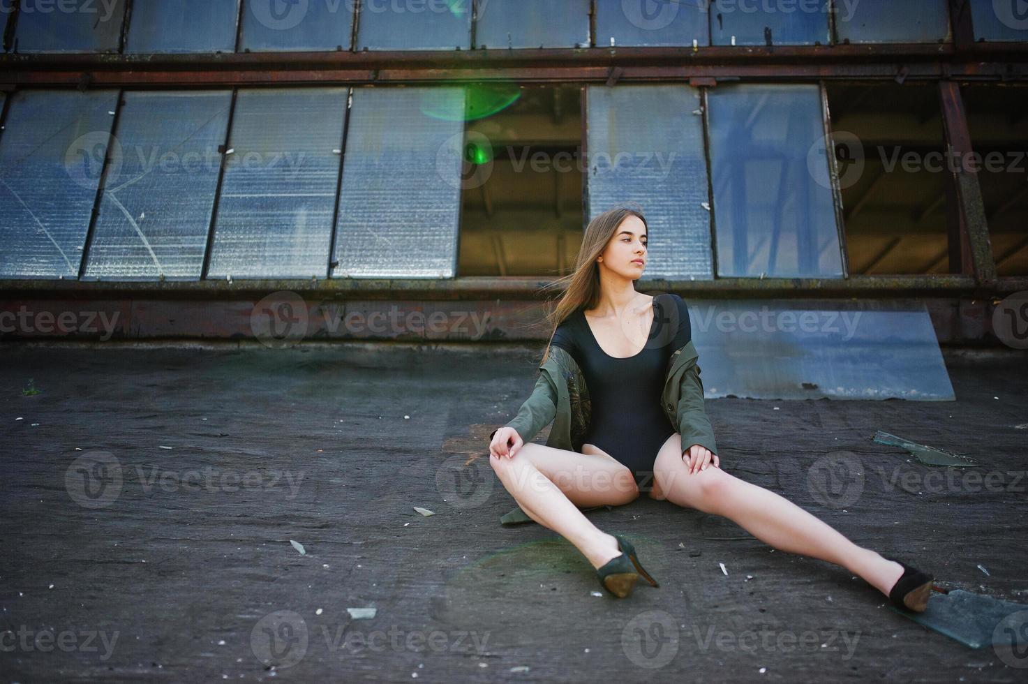 Sexy model girl wit long legs at black lingerie outfit body swimsuit combidress and jacket posed at the roof of abadoned industrial place with windows. photo