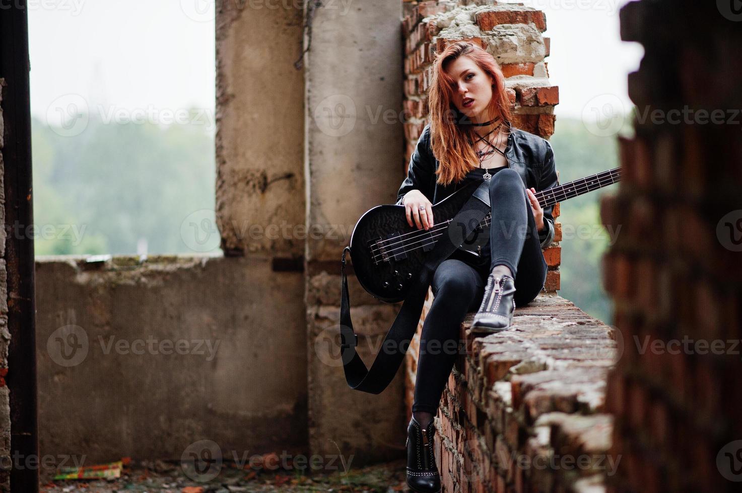 Chica punk pelirroja vestida de negro con bajo en un lugar abandonado. retrato de mujer gótica músico. foto