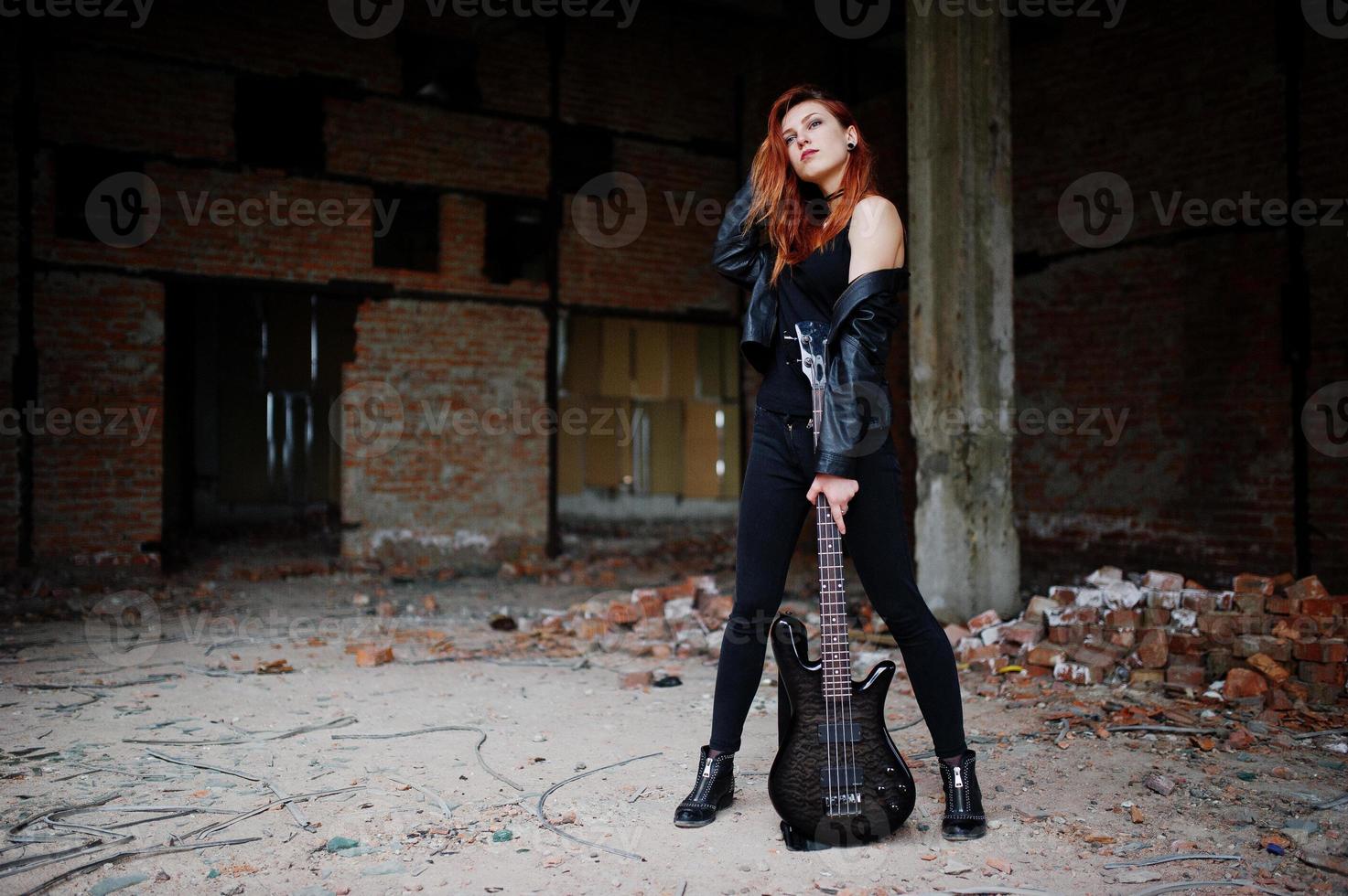 Red haired punk girl wear on black with bass guitar at abadoned place. Portrait of gothic woman musician. photo