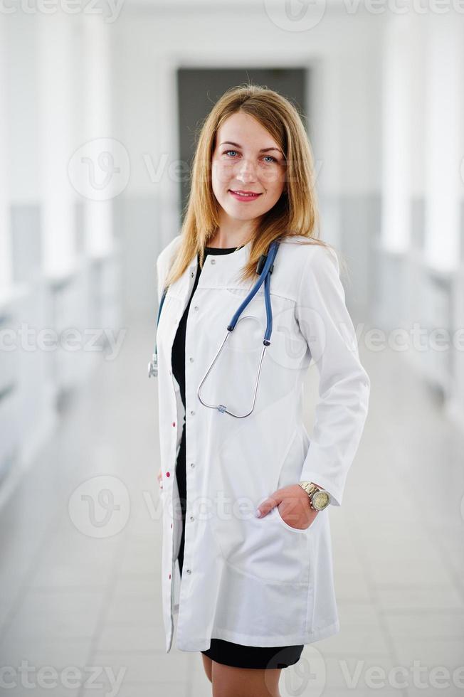 Portrait of a young attractive doctor in white coat with stethoscope posing in the hospital. photo