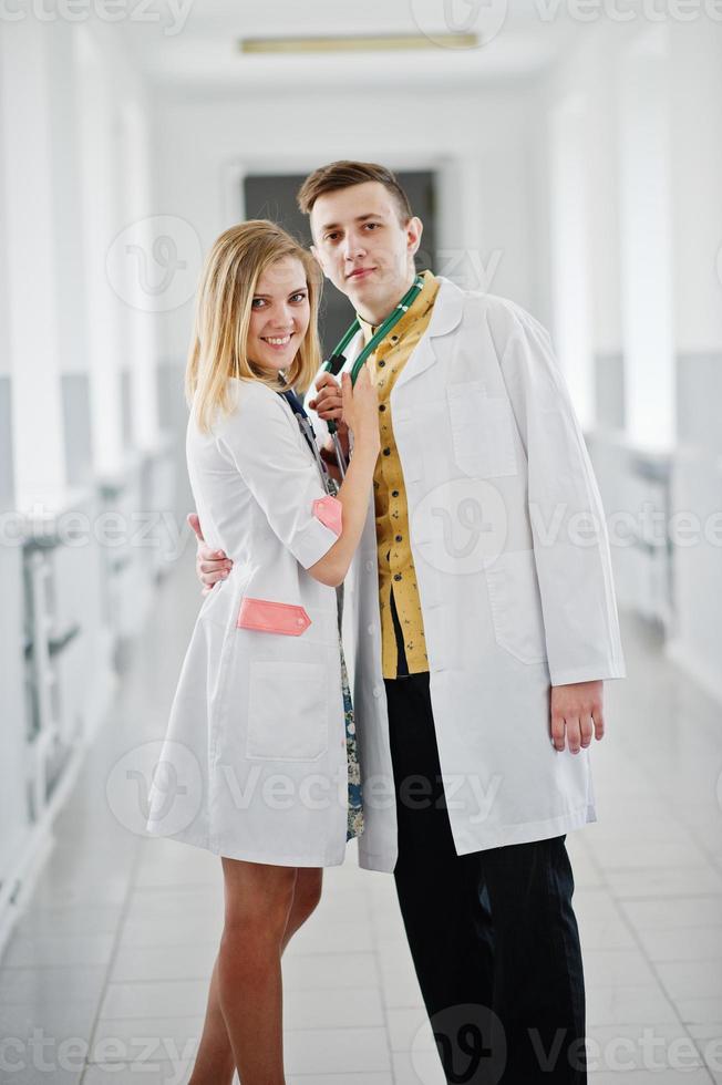 Two awesome doctors or medical workers wearing white coats pose with stethoscope in clinique or hospital. photo