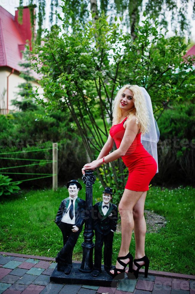 Gorgeous bride wearing red dress and veil posing outside at her bachelorette party. photo