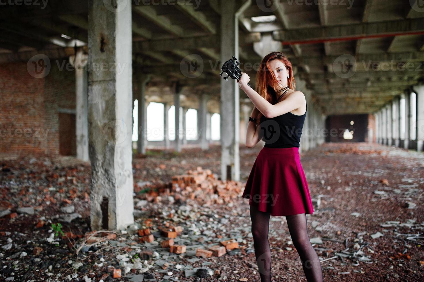 Chica punk pelirroja vestida con falda negra y roja, con bajo en un lugar abandonado. retrato de mujer gótica músico. foto