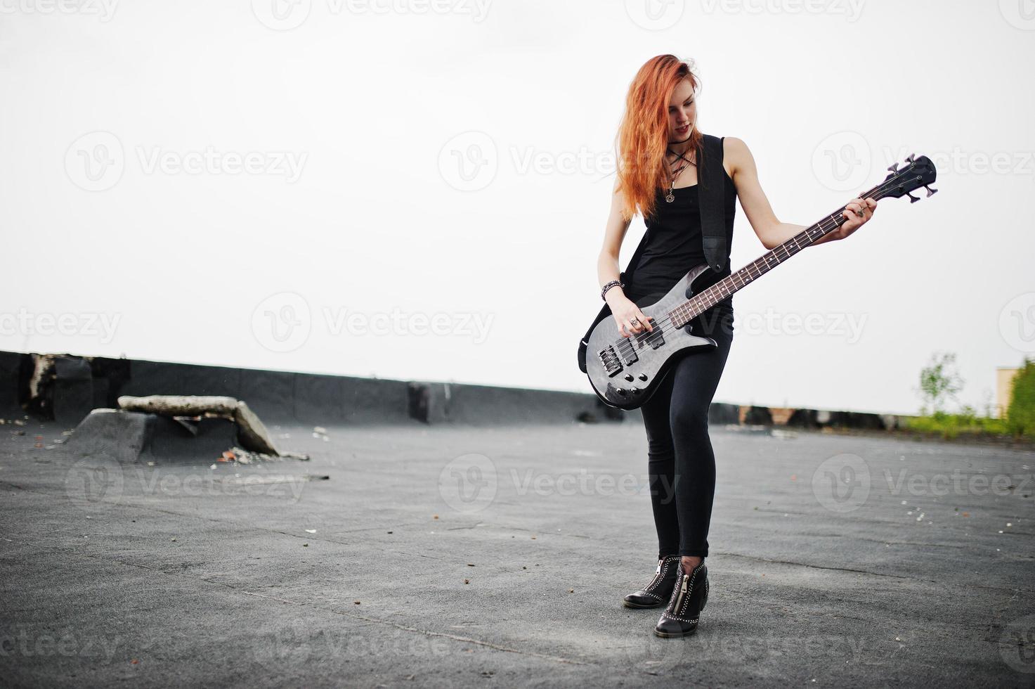 Red haired punk girl wear on black with bass guitar at the roof. photo