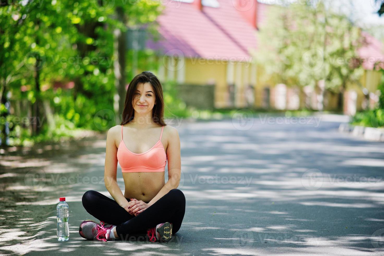 chica deportiva de fitness en ropa deportiva con botella de agua sentada en la calle en la calle, deportes al aire libre, estilo urbano. foto