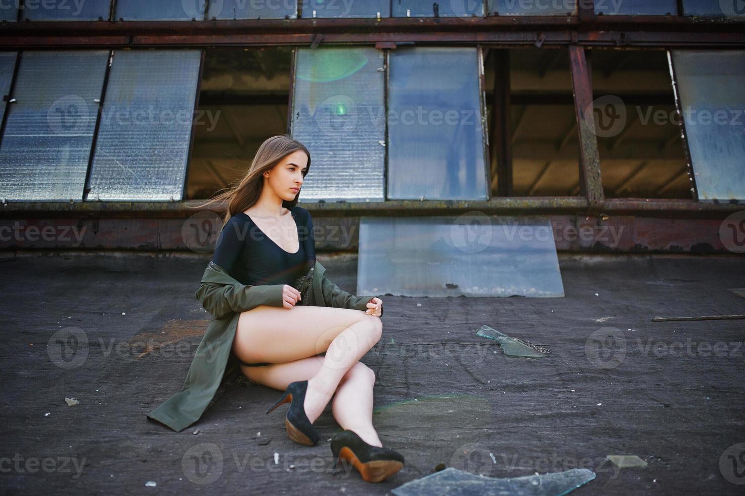 Sexy model girl wit long legs at black lingerie outfit body swimsuit combidress and jacket posed at the roof of abadoned industrial place with windows. photo