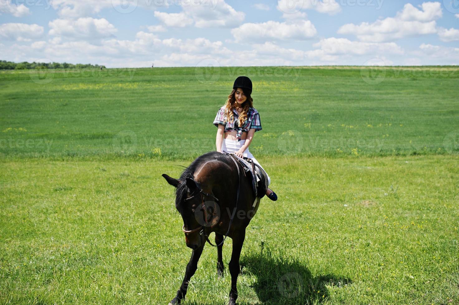 Young pretty girl riding a horse on a field at sunny day. photo