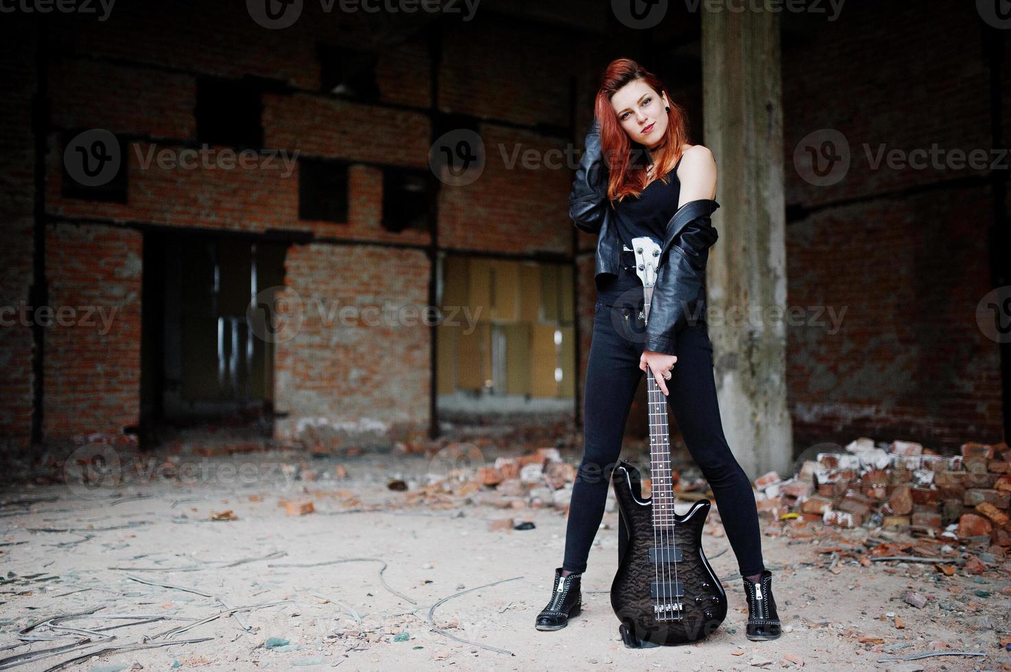 Red haired punk girl wear on black with bass guitar at abadoned place. Portrait of gothic woman musician. photo