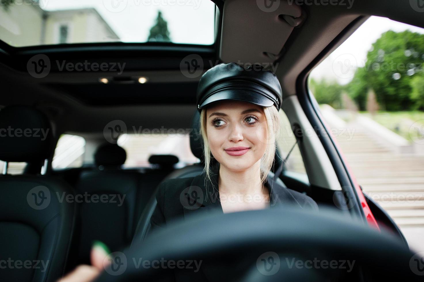 retrato de una hermosa modelo rubia de moda sexy con gorra y todo negro con maquillaje brillante, siéntate y conduce un coche rojo de la ciudad. foto