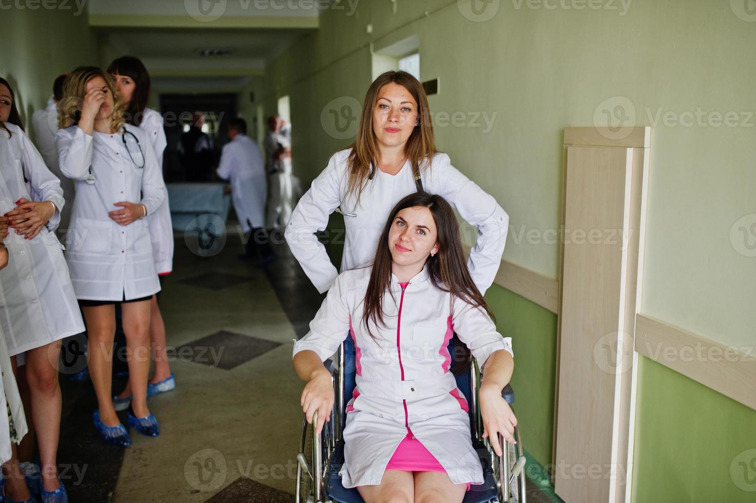 jóvenes médicos locos divirtiéndose posando en una silla de ruedas en el pasillo del hospital. foto