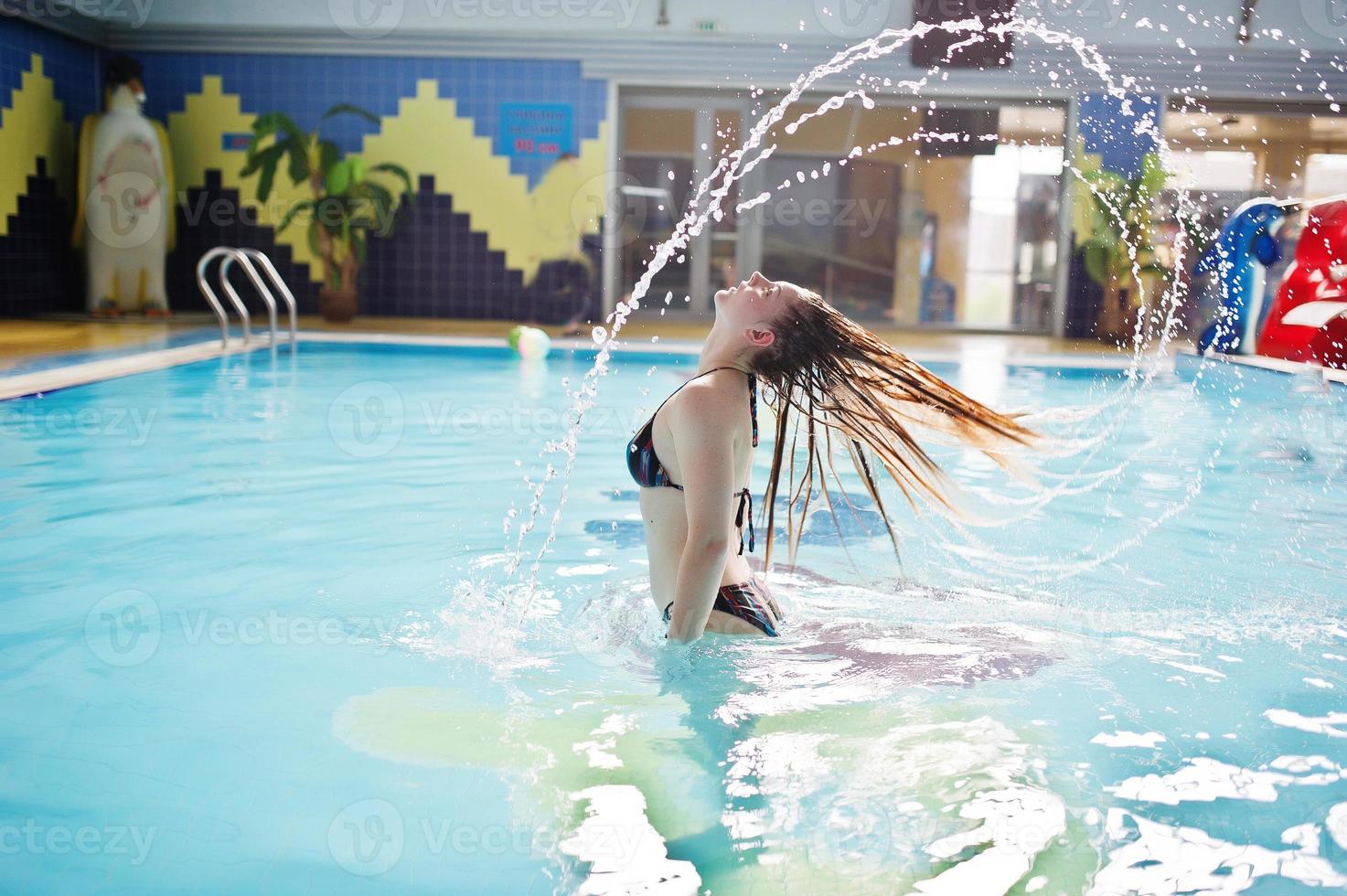 retrato de un hermoso firl en bikini haciendo un chapoteo con su cabello en la piscina en el parque acuático. foto