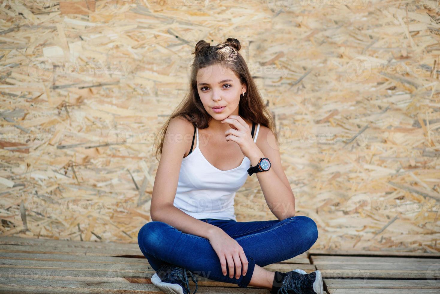 Portrait of a beautiful girl sitting on wooden boards against veneer wall. photo