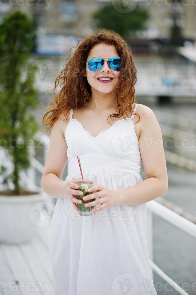 retrato de una joven atractiva posando con su cóctel en un lago con gafas de sol. foto