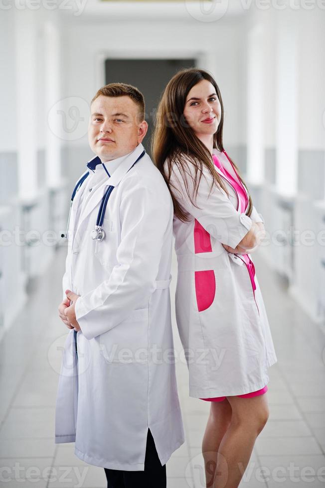 Two awesome doctors or medical workers wearing white coats pose with stethoscope in clinique or hospital. photo