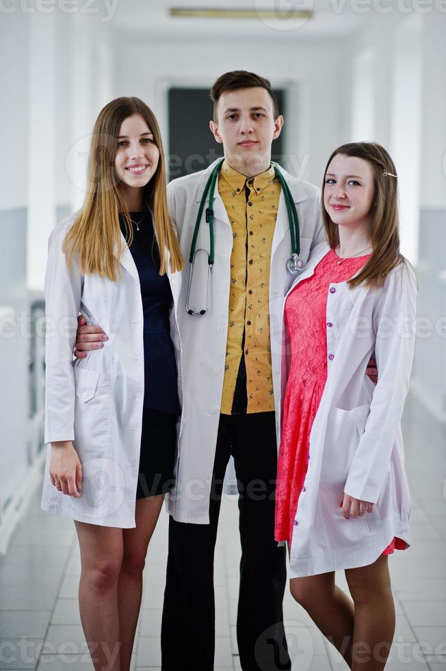 Two beautiful female doctors and one male in white coats posing in the hospital with stethoscope. photo