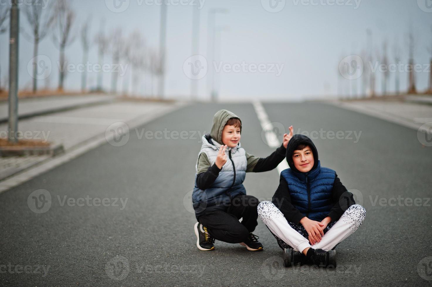 Brothers in hoodie sitting at center of road. photo
