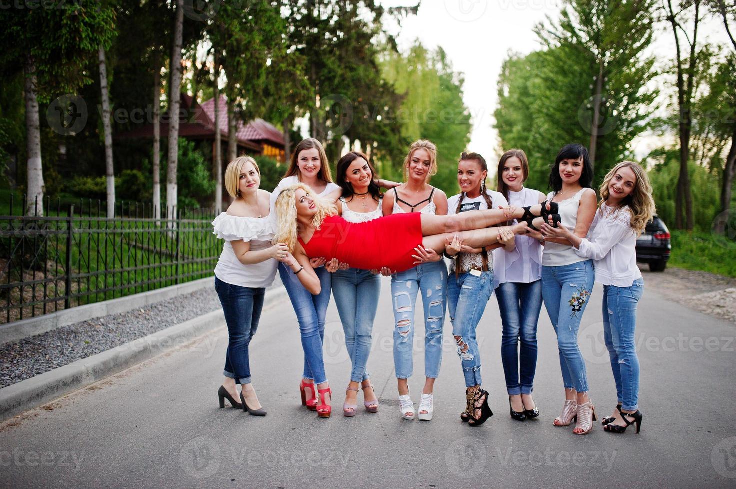 loca compañía de damas de honor sosteniendo a la novia con vestido rojo en el parque en la despedida de soltera. foto