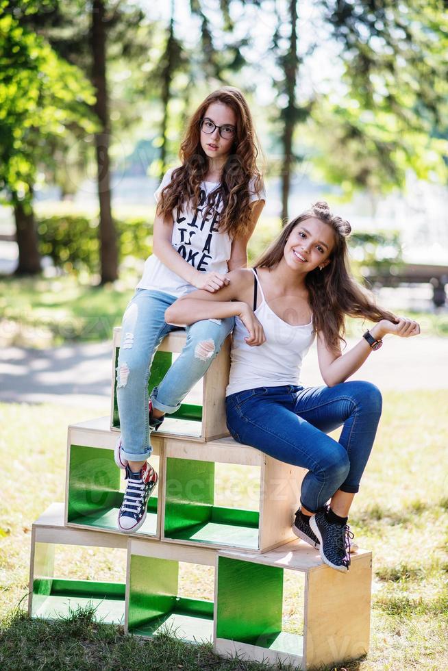 Two gorgeous young girls sitting on wooden boxes in the park on a sunny day. photo