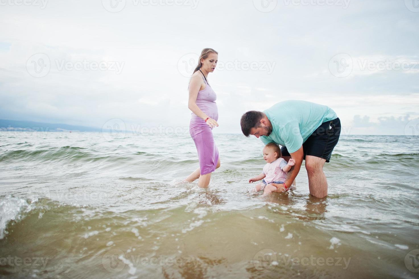 Summer vacations. Parents and people outdoor activity with children. Happy family holidays. Father, pregnant mother, baby daughter on sea sand beach. photo