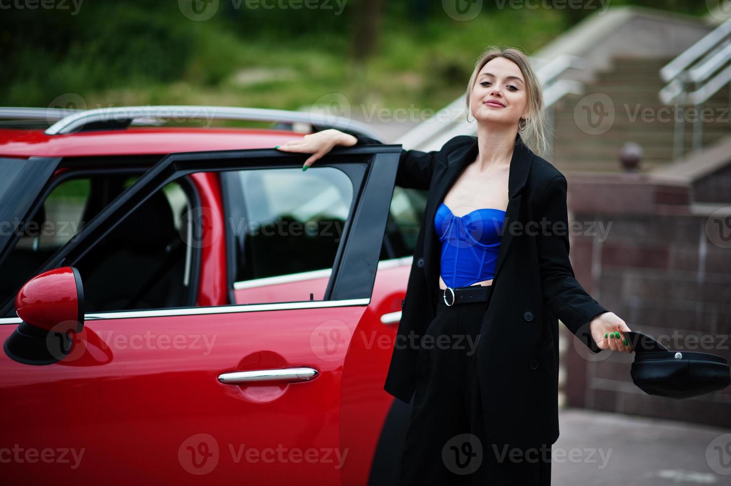 Portrait of beautiful blonde sexy fashion woman model in cap and in all black, blue corset, with bright makeup near red city car. photo