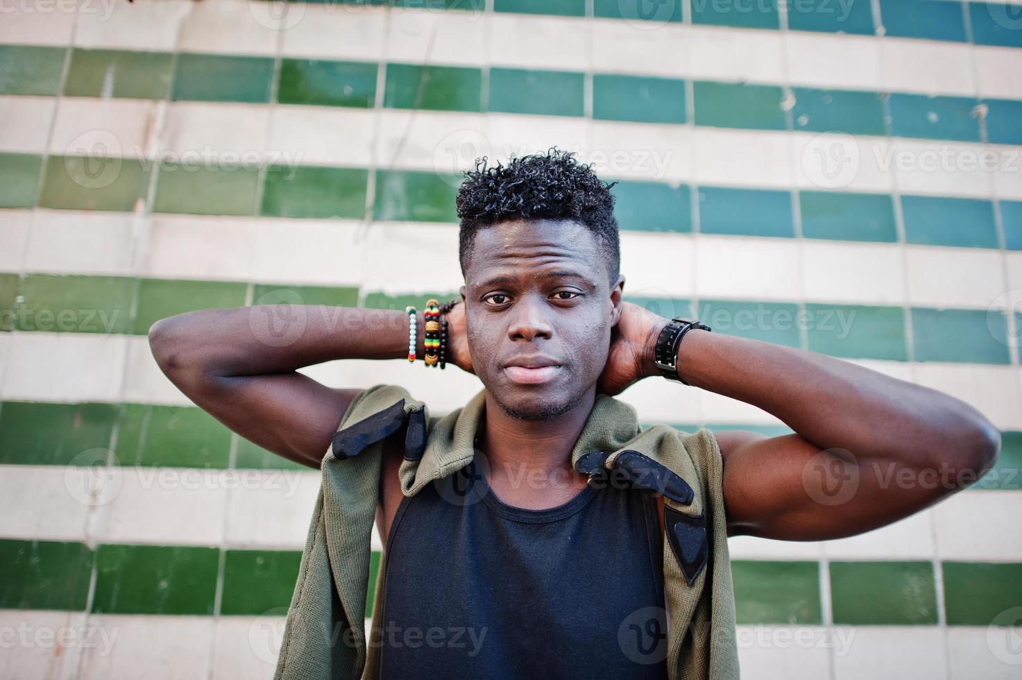 Attractive young african american guy in casual clothing standing next to the tiled wall. photo