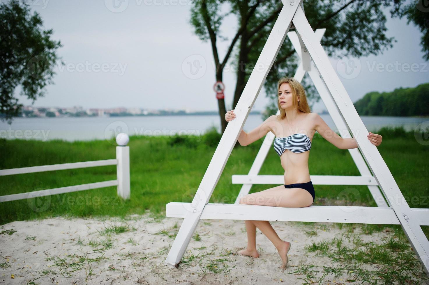 retrato de una atractiva modelo femenina posando junto a la construcción triangular de madera blanca en el parque con un lago al fondo. foto