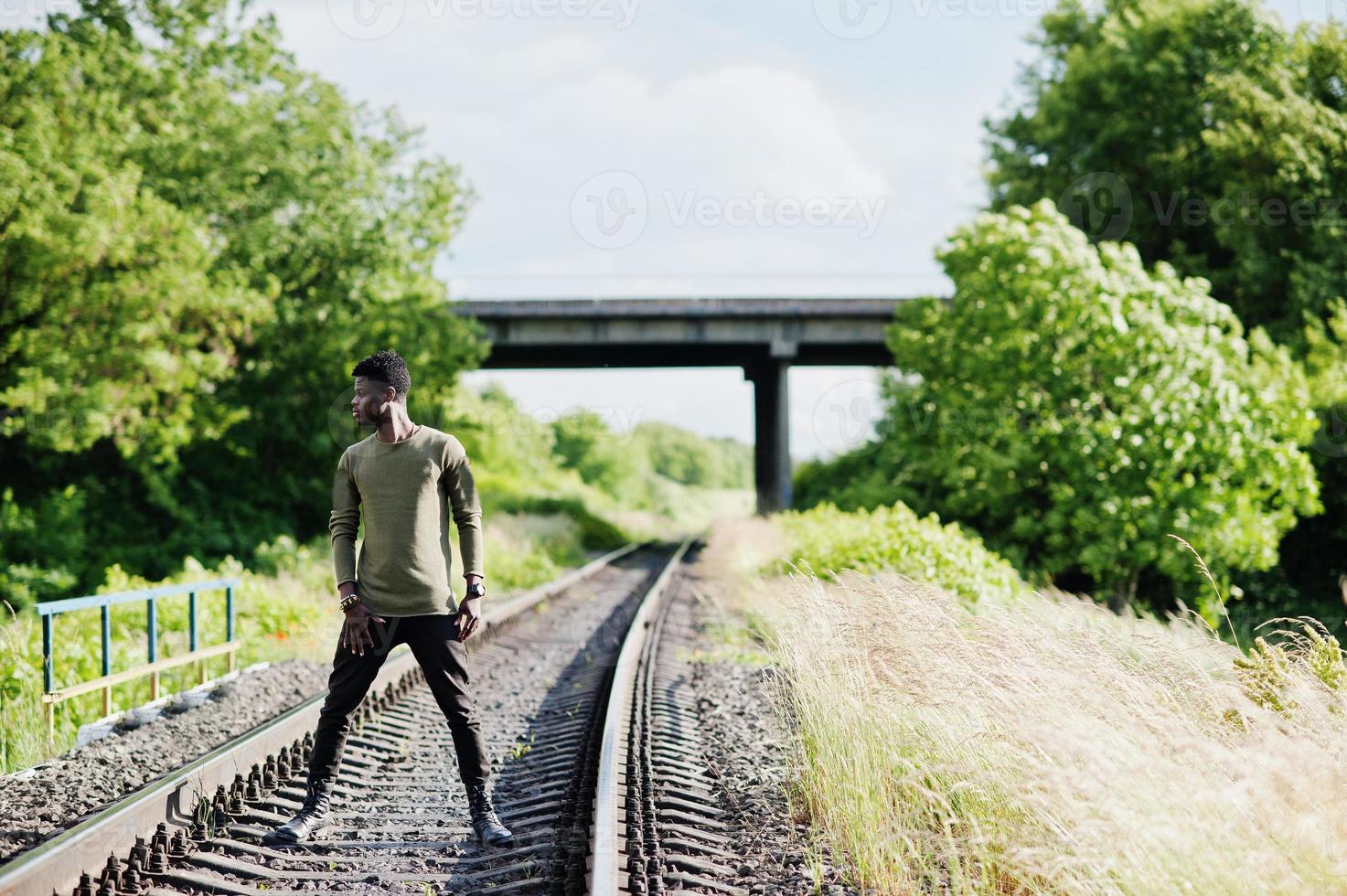Cool black african american man walking and posing on railway in the countryside. photo