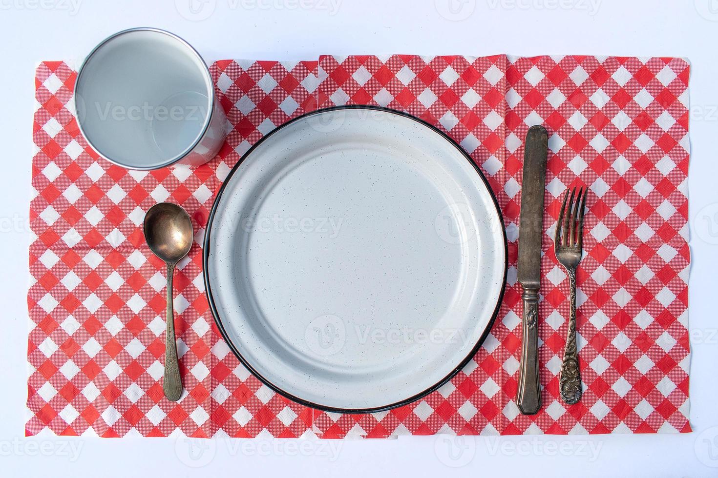 flat lay picnic table place setting of plate, cup, silverware, and checkered tablecloth photo