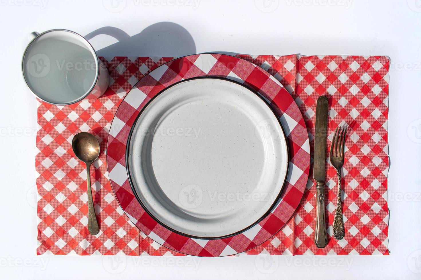 flat lay picnic table place setting of plate, cup, silverware, and checkered tablecloth photo