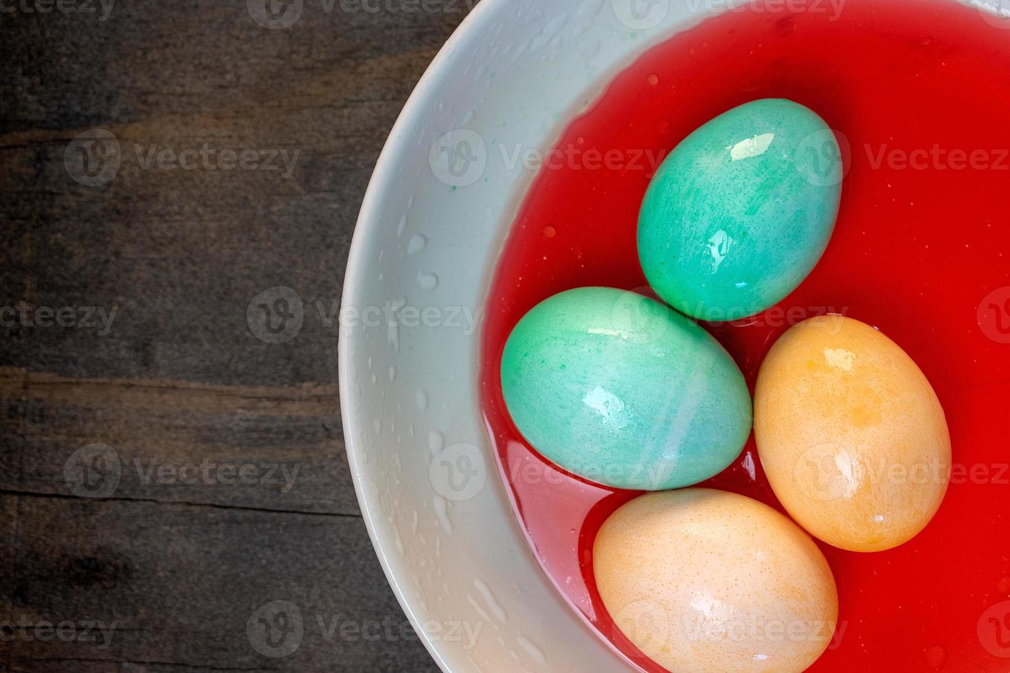 top view of bowl of red color dye with colored Easter eggs in it photo