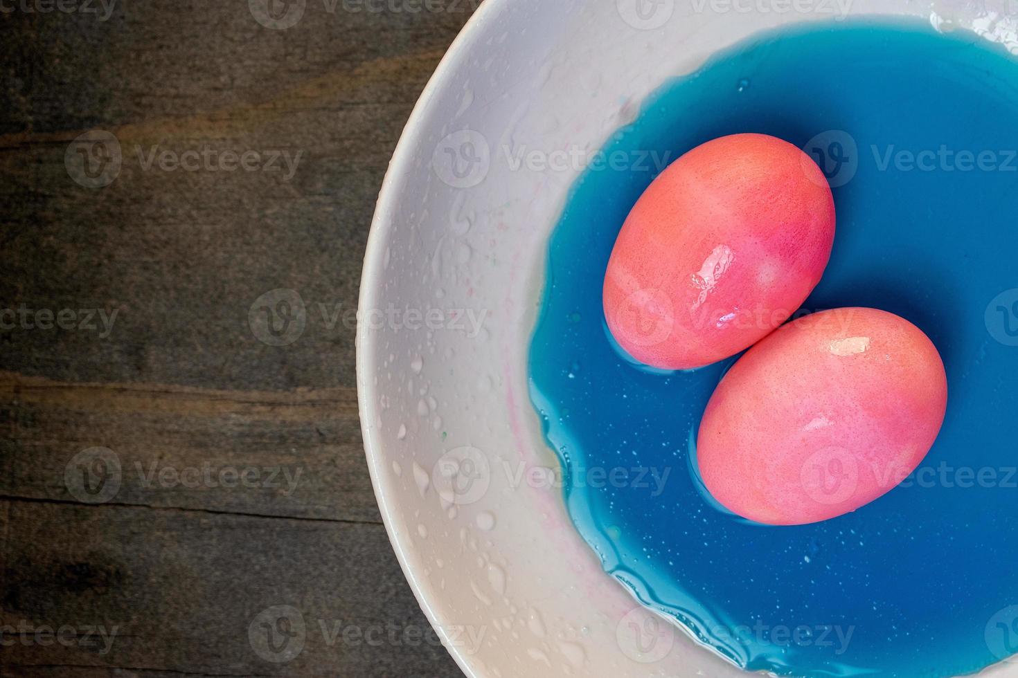 top view of bowl of blue color dye with colored Easter eggs in it photo