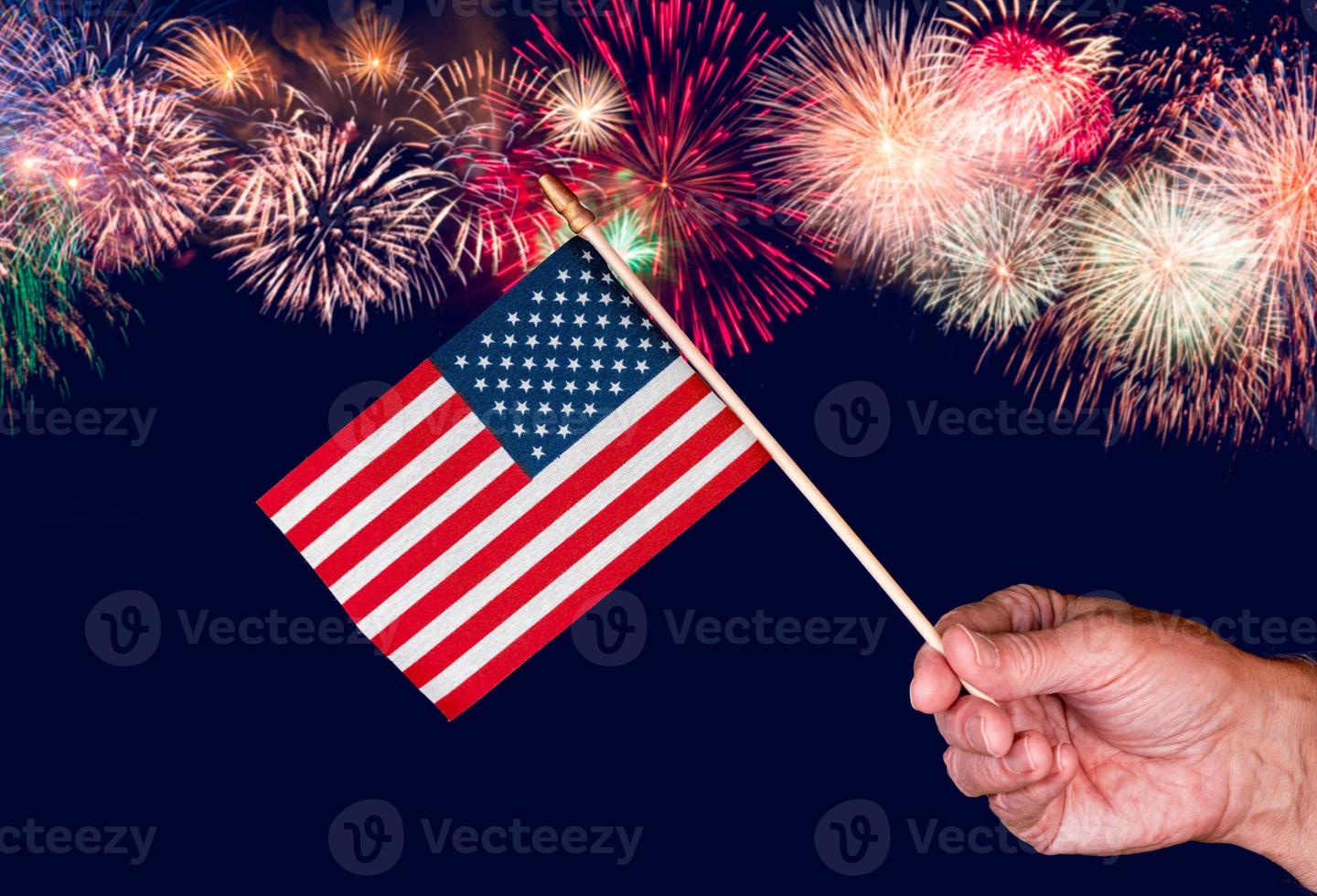 Senior man hand holding a small USA flag against fireworks background photo